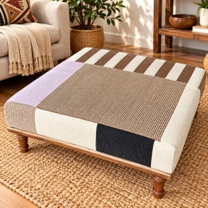 Pode incluir: Um otomano quadrado com um design de patchwork apresentando um grande painel central castanho texturizado, secções em creme, um bloco de canto lavanda, um detalhe retangular preto e bordas às riscas castanhas e creme sobre pés de madeira.