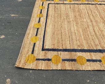 Puede incluir: Una alfombra rectangular con aspecto de fibra natural. La alfombra presenta un borde azul marino con acentos circulares amarillos. La textura de la alfombra es visible y el diseño es simple y moderno. Adecuado para uso en interiores.