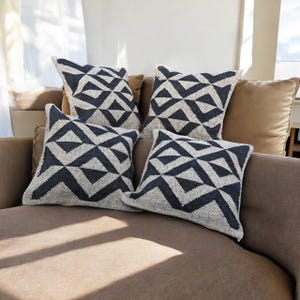 May include: Four square throw pillows with a geometric pattern in black and off-white. The pillows are arranged on a brown sofa, creating a modern and stylish look for home decor.