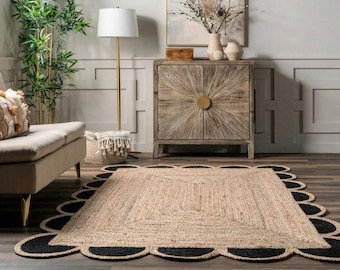 May include: A rectangular jute rug with a scalloped black border. The rug has a natural beige color in the center and is placed on a dark wood floor. The room also features a sofa, cabinet, and a floor lamp.