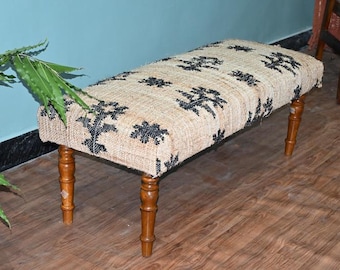 Puede incluir: Banco rectangular con una parte superior de tejido natural con un estampado floral negro. El banco tiene cuatro patas de madera con acabado marrón oscuro. El banco está sobre un suelo de madera.