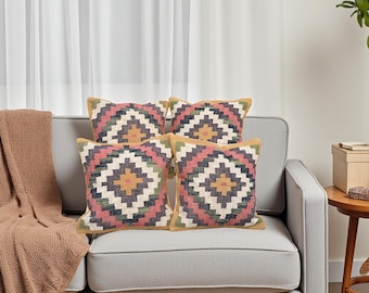 Könnte beinhalten: Vier dekorative Zierkissen mit geometrischen Mustern in Rosa, Grün, Gelb und Grau liegen auf einem grauen Sofa. Die Kissen haben einen gelben Rand. Eine braune Decke ist über dem Sofarücken drapiert.