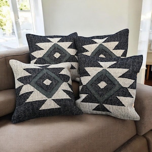 May include: Four decorative throw pillows with a geometric pattern. The pillows feature a dark gray background with a cream and teal diamond and triangle design. The pillows are arranged on a neutral-colored sofa.
