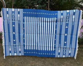 May include: A blue and white patterned textile with a rectangular design. The textile features vertical white stripes in the center and along the sides, with geometric patterns and fringe edges. The color scheme is primarily blue and white.