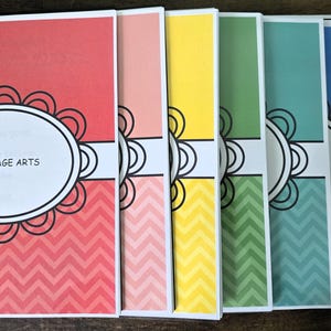 May include: A collection of spiral-bound notebooks with colorful covers. The first notebook is red with a white oval label that reads "LANGUAGE ARTS". The covers feature a chevron pattern and a decorative floral design. Other notebooks are pink, yellow, green, blue, and purple.