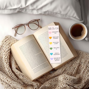 May include: An open book with a bookmark labeled "Bible Color Code" lies on a beige knitted blanket. A pair of eyeglasses and a cup of coffee are also present. The bookmark lists different categories with corresponding colors.