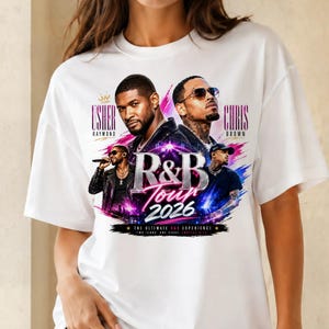 May include: A white t-shirt featuring a graphic print of Usher Raymond and Chris Brown. The design includes the text "R&B Tour 2026", "The Ultimate R&B Experience", and "Two Icons, One Stage, Endless Hits" with colorful pink and blue brushstroke accents.