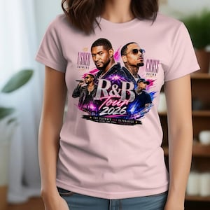 May include: A light pink t-shirt featuring a graphic print of musical artists Usher and Chris Brown. The design includes the text R&B TOUR 2026, Usher Raymond, and Chris Brown, set against a vibrant background of blue and pink light streaks.