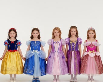 Puede incluir: Cinco niñas con disfraces de princesas, cada una con un vestido diferente. Los vestidos son de varios colores, incluyendo amarillo, azul, morado y rosa, con detalles decorativos. Cada niña lleva una diadema o corona a juego.