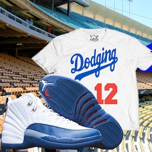 May include: White and blue sneakers with a blue and red sole are displayed next to two t-shirts. One t-shirt is white, the other is blue. Both shirts have the word "Dodging" in script and the number "12" in red.