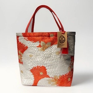 以下が含まれることがあります： 鮮やかなオレンジとシルバーの花柄の刺繍が施されたトートバッグ。赤いハンドルが2本付いており、赤い紐で結ばれた茶色の長方形の紙タグには「AYUKO TOKYO」の文字と円形のロゴが印刷されています。