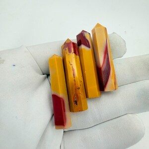 May include: Four polished crystal points arranged in a row, each featuring a smooth, hexagonal shape. The stones display a distinct colour palette of vibrant mustard yellow and deep maroon red, with natural veining patterns visible on the surfaces.