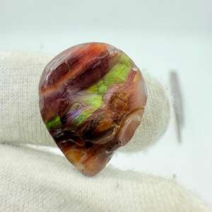 May include: A polished, iridescent gemstone with a mix of colors, including red, green, and brown. The stone has a smooth, glossy surface and a unique, organic shape. The gemstone is likely a decorative item or a piece of jewelry.
