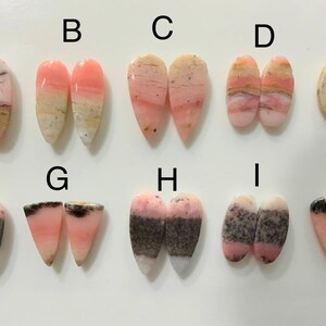 Puede incluir: Una colección de diez pares de cabujones de piedras preciosas pulidas, cada uno con un patrón único. Las piedras muestran una gama de colores, incluyendo rosa, blanco y marrón, con variaciones en vetas y veteado. Las formas son en su mayoría de lágrima u ovaladas.