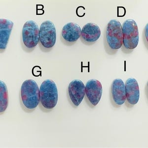 Peut inclure: Présentation de dix paires de pierres précieuses polies de formes variées, dont ovales, en goutte et en cœur. Les pierres présentent une couleur de base bleue avec des veines rouges et roses, sur fond blanc.
