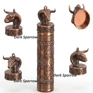 May include: Bronze-colored decorative container with a cobra head lid. The container has an ornate, embossed design. The text "Dark Sparrow" is visible on the container. The cobra head has horns and a loop for hanging.