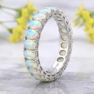 Può includere: Un anello eternity in argento con una fila continua di opali ovali iridescenti montati a griffe. L'interno dell'anello reca chiaramente l'incisione SILVER 925, che indica la composizione metallica di questo gioiello di forma circolare.