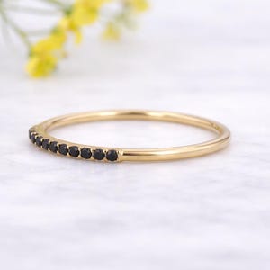 May include: A gold ring featuring a row of small, black gemstones. The ring is set against a white marble surface, with a blurred background of yellow flowers.
