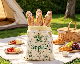 May include: A cream-coloured fabric bread bag featuring a botanical print of green herbs and purple lavender, with the name Sophie printed in green script. The bag is filled with three crusty baguettes and has a pale yellow interior lining.