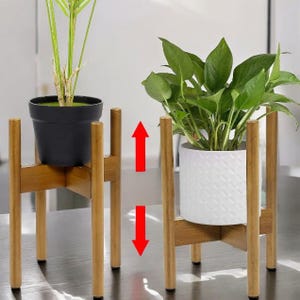 May include: Two adjustable wooden plant stands. One stand holds a black pot with a green plant, the other holds a white patterned pot with a green plant. The stands have a natural wood finish and are designed to elevate plants.
