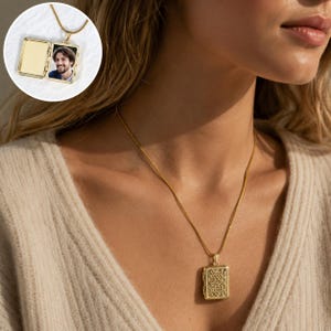 May include: A gold-toned rectangular locket pendant on a matching chain. The locket features an intricate filigree pattern on the front. An inset shows the locket opened to reveal a blank left side and a photograph of a smiling man on the right.