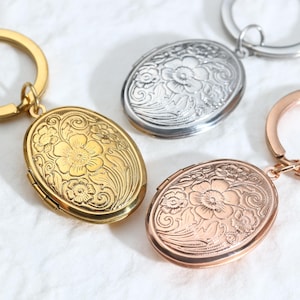 May include: Close-up of three oval lockets with floral designs. One is gold, one is silver, and the other is rose gold. Each locket is attached to a keyring. The lockets have an engraved floral pattern.