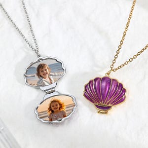 May include: Two seashell-shaped pendant necklaces. One is silver with a hinged locket containing two photos. The other is gold with a purple enamel seashell pendant. Both necklaces have delicate chains.