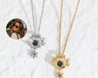May include: Two necklaces with thin metal chains and circular pendants featuring a central dark stone and a small star-shaped charm with a purple accent. One pendant is silver-toned, and the other is gold-toned. A circular inset shows a person wearing the necklace.