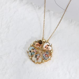 May include: A gold-colored necklace with a pendant shaped like a four-leaf clover. Each heart-shaped leaf holds a small photo. The necklace has a delicate chain and is adorned with small, clear crystals.