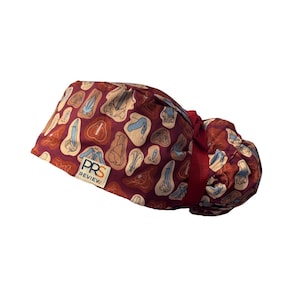 Puede incluir: Un gorro quirúrgico burdeos con un patrón repetido de formas abstractas en beige, azul y marrón. El gorro tiene una cinta roja y una etiqueta que dice "PRS REVIEW".
