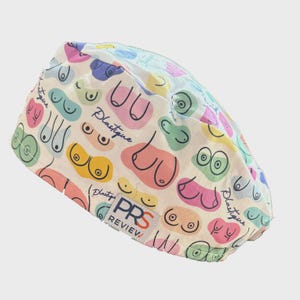 May include: A white surgical scrub cap with a colorful pattern of stylized breasts in various shapes and colors. The cap has the word "Plastique" in cursive and a "PRS REVIEW" label.