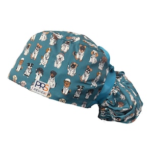 May include: A teal scrub cap featuring a repeating pattern of various dog breeds dressed in white veterinarian coats and stethoscopes. The cap includes a gathered back with teal ribbon ties and a white rectangular label reading PRS REVIEW.