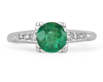 May include: A silver ring featuring a round, green emerald gemstone set within a halo of smaller, clear gemstones.