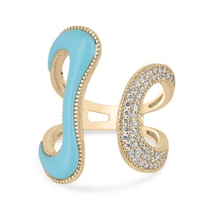 Op de afbeelding: Een goudkleurige ring met een lichtblauwe emaille accent en een band bezet met kleine, heldere edelstenen. De ring heeft een open ontwerp met gebogen elementen.