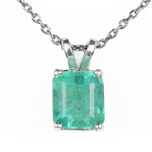 May include: A silver necklace featuring a rectangular emerald pendant. The emerald is a vibrant green color and is set in a silver bezel. The chain is a delicate silver link chain. The pendant is centered on a white background.