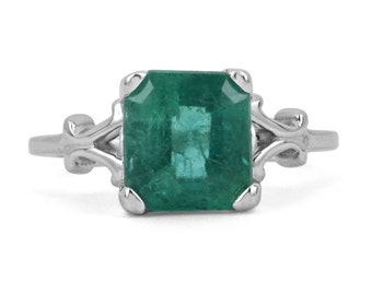 May include: A silver ring with a square emerald green gemstone set in a delicate, ornate setting.