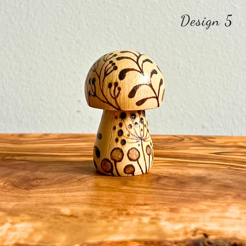May include: A wooden mushroom figurine with a light brown cap and stem. The cap features a dark brown floral design, while the stem has a dotted and circular pattern. The text "Design 5" is in the upper right corner.