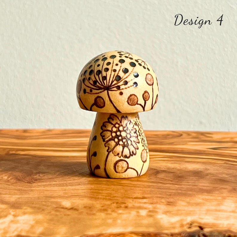 May include: A wooden mushroom figurine with a light brown finish and intricate floral designs. The mushroom cap features a pattern of small black dots and a larger floral design. The text "Design 4" is visible in the upper right corner.