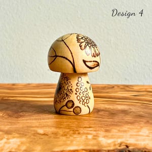 May include: Wooden mushroom figurine with intricate etched designs. The mushroom cap features a floral pattern and the stem has a dotted design. The text "Design 4" is visible in the upper right corner. The figurine is on a wooden surface.