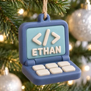May include: A blue laptop-shaped Christmas ornament featuring a light blue screen with white code brackets and the name ETHAN in white letters. The keyboard area has six white square keys. A jute twine loop is attached to the top for hanging.