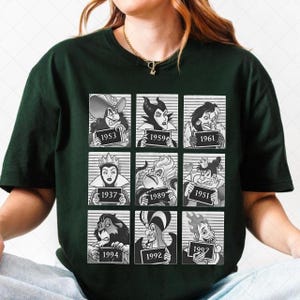 May include: Dark green t-shirt featuring a grid of nine cartoon villains, each holding a sign with a year. The villains are in black and white, set against a striped background. The years range from 1937 to 1997.