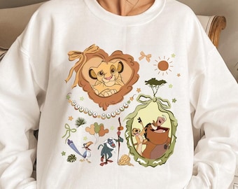 Può includere: Felpa bianca con una grafica colorata dei personaggi de Il Re Leone. Il design include Simba, Timon, Pumbaa e Zazu, con le parole "Hakuna Matata". Il design è circondato da elementi decorativi.