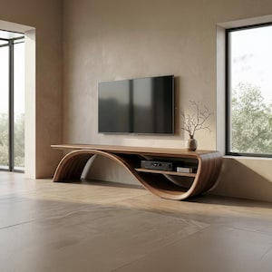 May include: A curved wooden media console with a smooth, continuous wave-like frame. The unit features a flat top surface, a lower storage shelf holding electronic devices, and a small vase with bare branches placed on the right side.