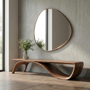 May include: A long, low-profile wooden bench with a smooth, curved, continuous base design. A clear glass vase containing green leafy branches sits on the bench. Above the bench hangs an asymmetrical, organic-shaped mirror with a thin gold frame.