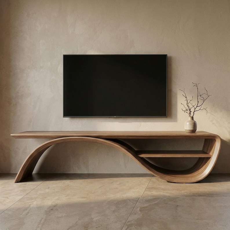 May include: A long, curved wooden media console with a smooth, flowing silhouette and a single integrated shelf. A flat-screen television is mounted on the wall above the console, and a small ceramic vase with bare branches sits on the right.