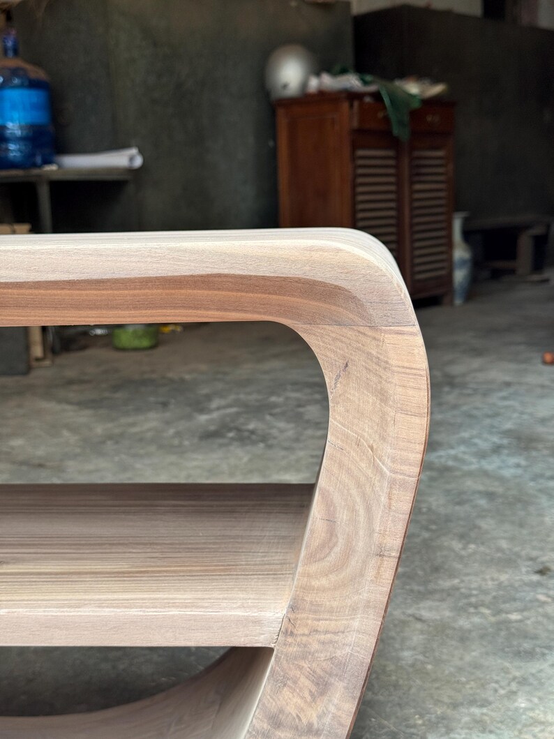 May include: A light brown wooden side table featuring a smooth, curved edge design with visible natural wood grain patterns. The table includes a flat top surface and a lower shelf, connected by a continuous, rounded side frame structure.