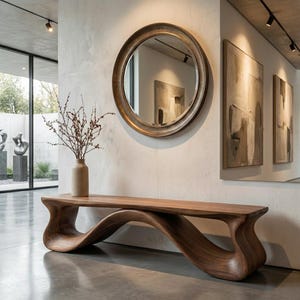 May include: A long, low-profile wooden bench with a continuous, fluid, wave-like base crafted from dark walnut-toned wood. The bench is positioned beneath a large, circular wall mirror with a thick, dark frame and a tall, light-coloured ceramic vase.