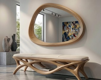 May include: A wall-mounted mirror with an irregular, organic-shaped light wood frame, positioned above a long bench featuring a light-colored upholstered seat and a complex, interconnected light wood base with a lower shelf for storage.