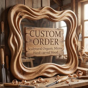 Puede incluir: Un espejo orgánico escultórico tallado a mano con un marco único y fluido. El espejo tiene un acabado de veta de madera natural y presenta las palabras "CUSTOM ORDER" en un letrero de madera. Se ven herramientas de tallado y virutas de madera.
