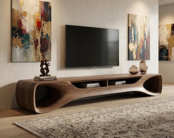 May include: A long, low-profile walnut wood media console with a curved, organic silhouette featuring open side compartments and central shelving. The unit holds a flat-screen television, a bronze sculpture, and several books.